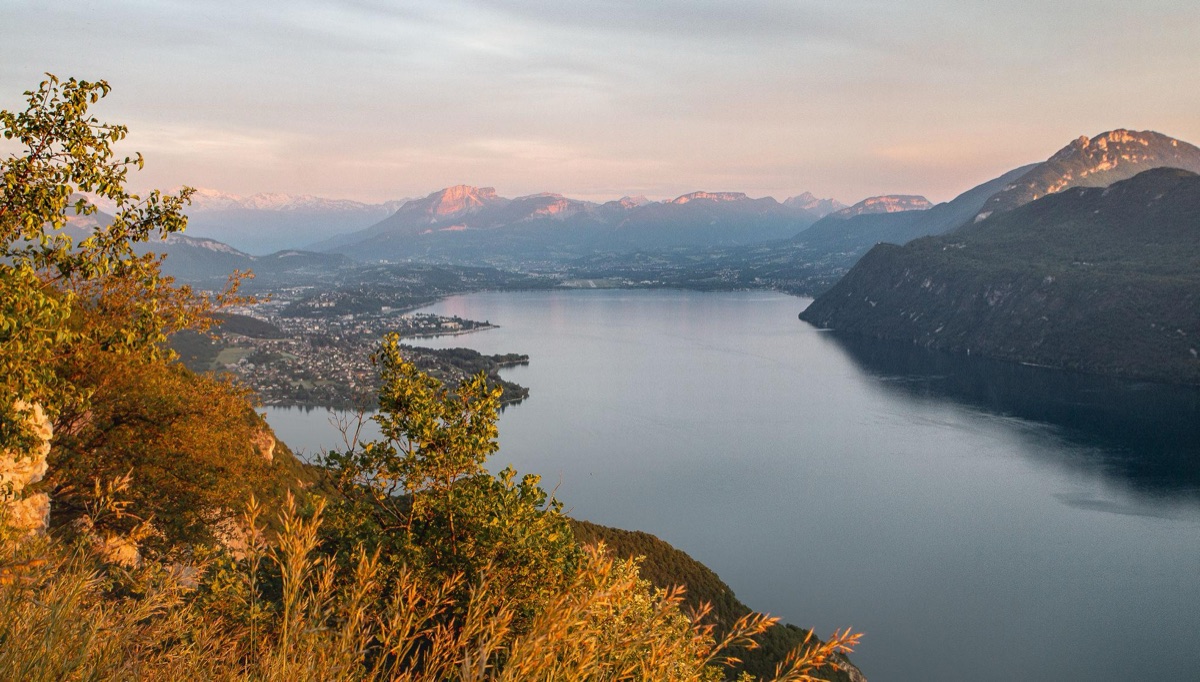 Lac alpin entouré de forêts et de montagnes au soleil couchant